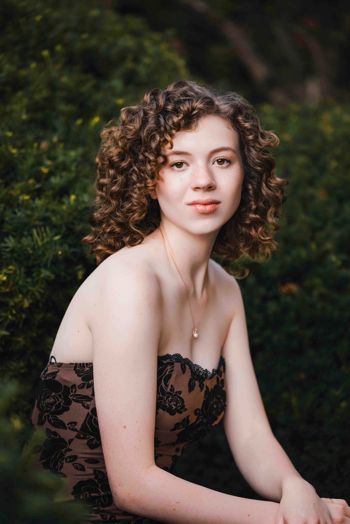 Senior girl with curly hair, elegantly posed outdoors in soft evening light.