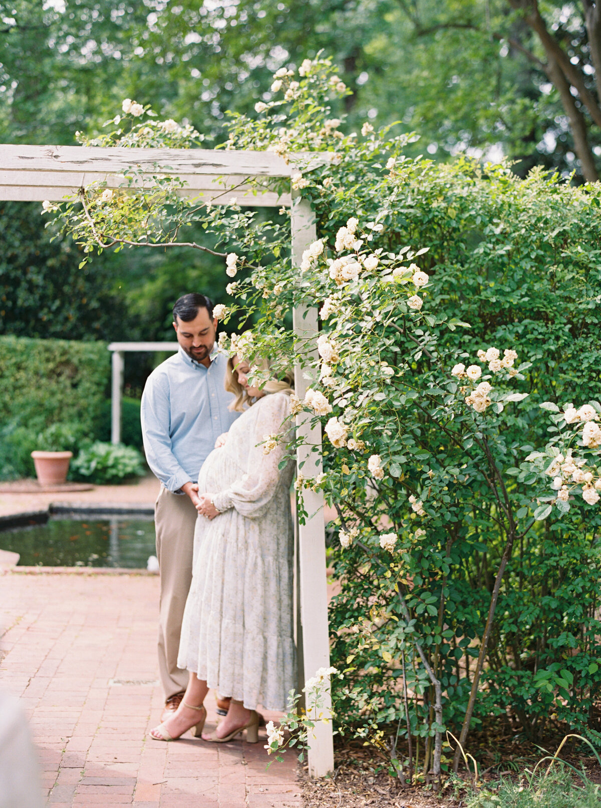Expecting parents lean against a flowering trellis. Image by Raleigh maternity photographer A.J. Dunlap Photography.