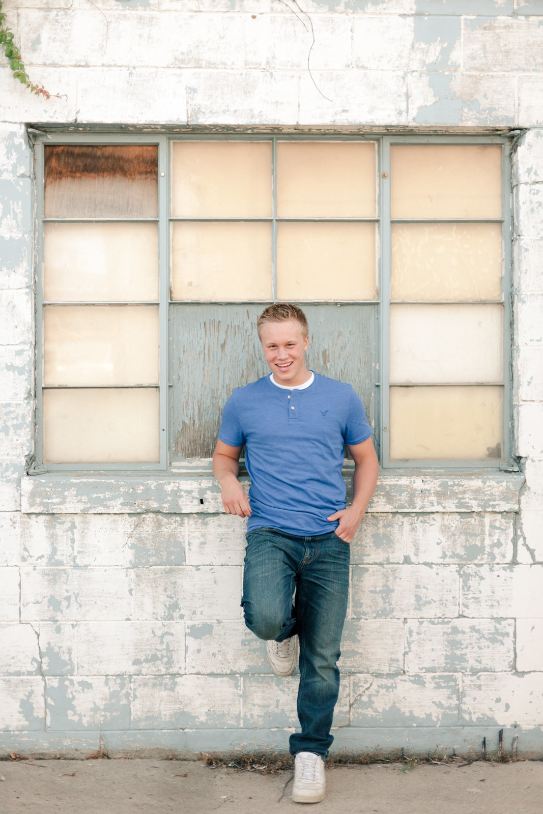 senior guy leans against rustic industrial building chipped paint and windows