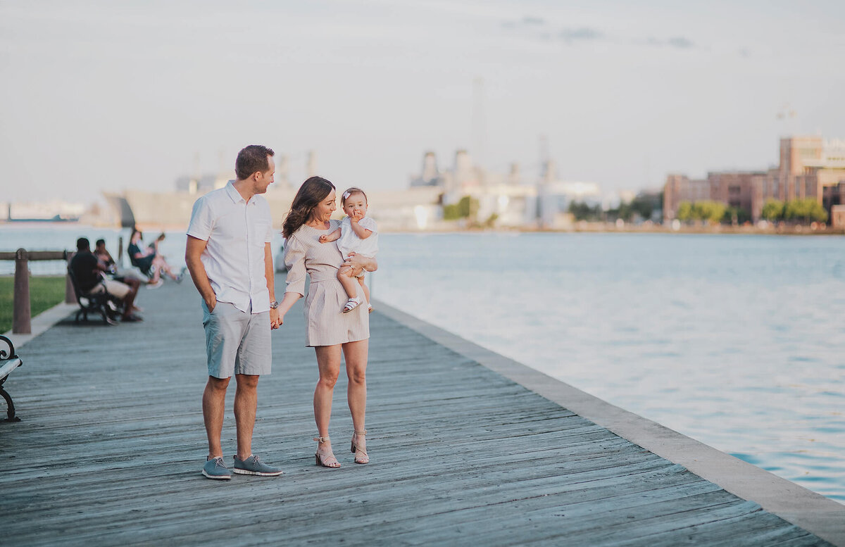 Mother and father with baby girl holding hands on a pier in Fells Point Baltimore Maryland