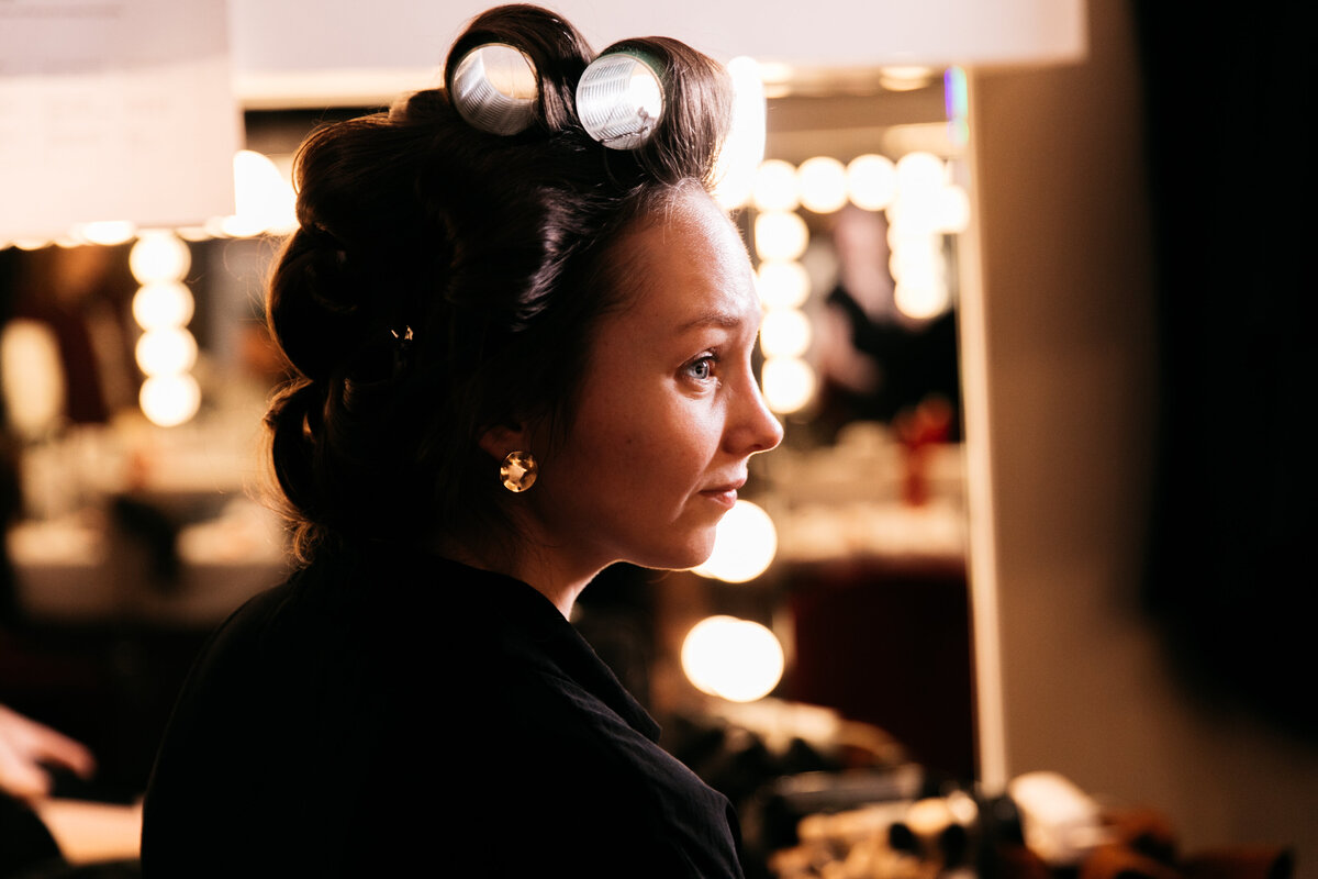 Portret van brunette vrouw met krullers in haar haar voor theaterspiegel.