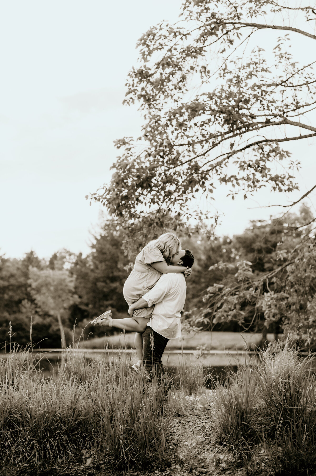 arkansas engagement photos with man picking up his fiance as she leans in to kiss him in front of a lake