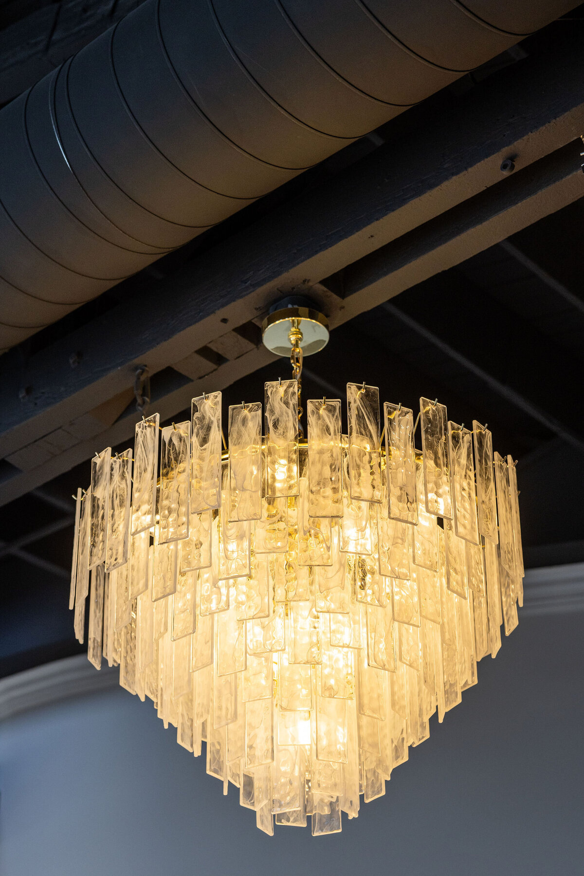 Close-up of an exquisite crystal chandelier accenting the Happy Hour space, adding elegance and attention to detail within original exposed industrial ceilings and natural light