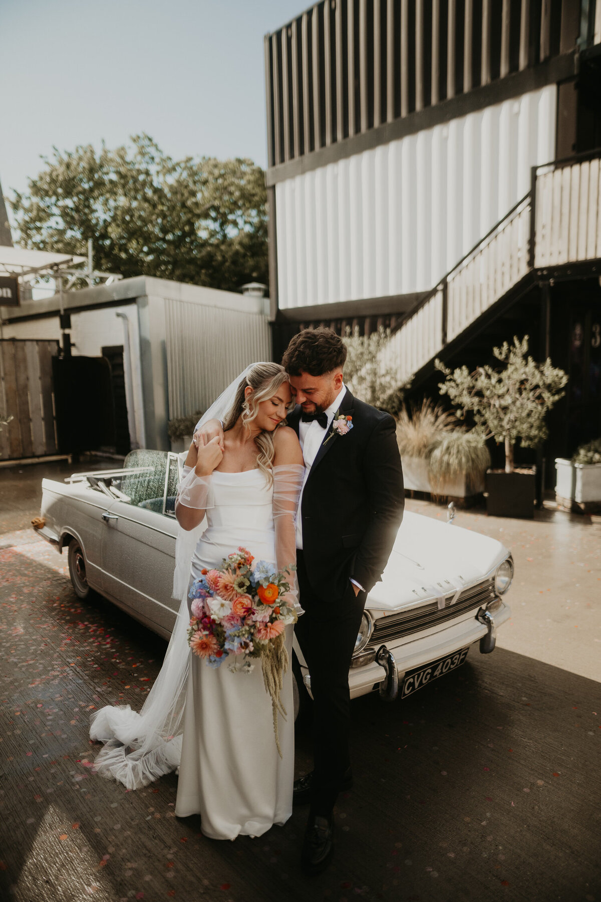 Bride and groom sit on a vintage Triumph car at their wedding at The Shack Revolution. 