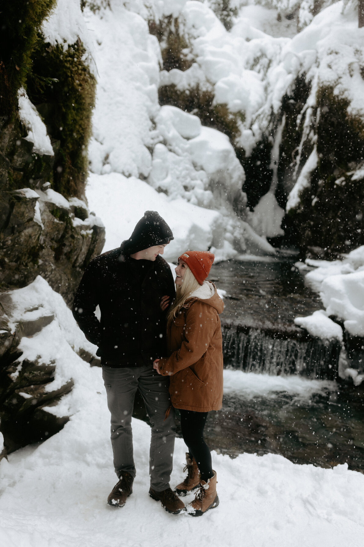Couple standing together next to a snow covered waterfall.