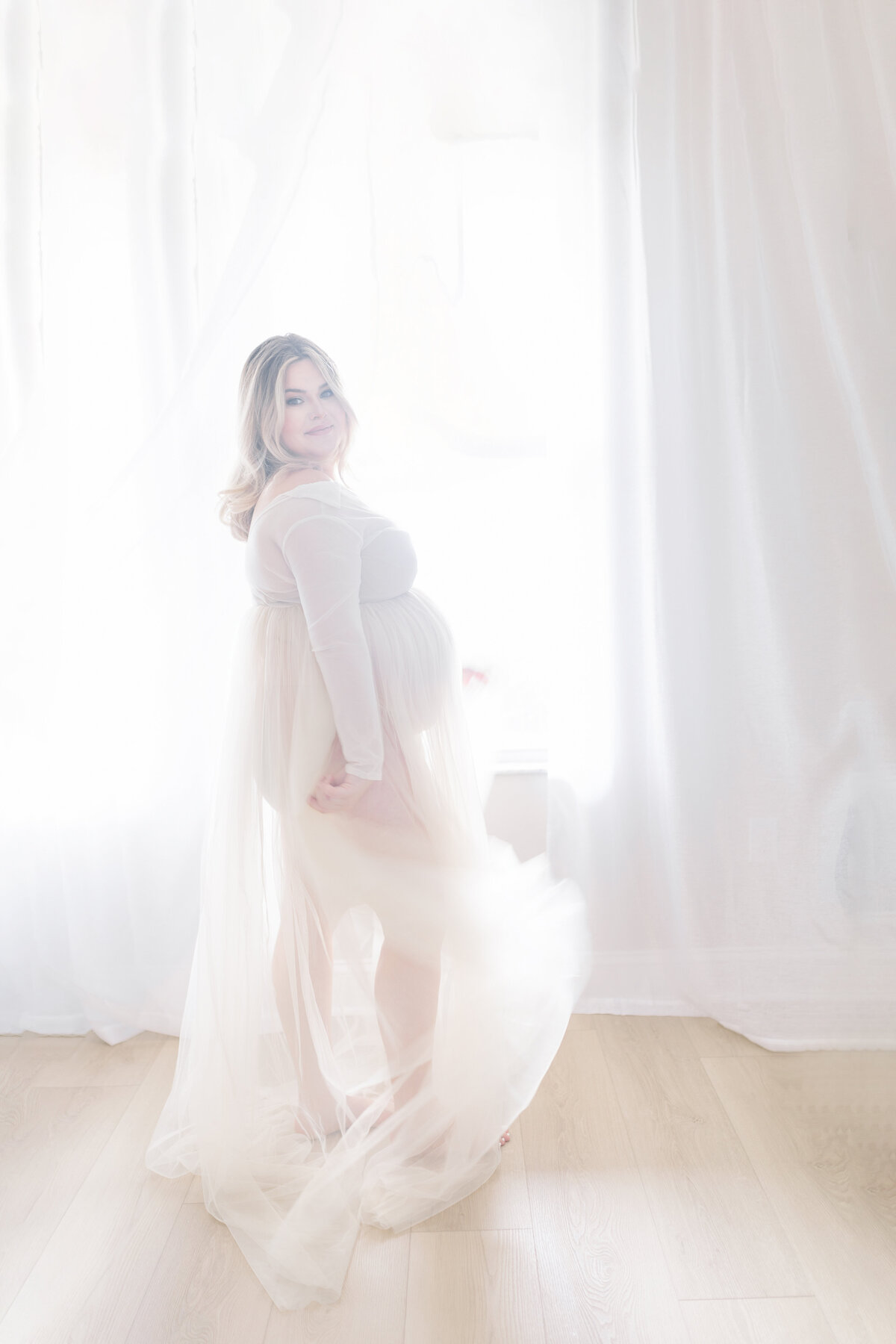 Graceful Tampa maternity portrait of mom-to-be in flowing cream gown with warm natural light