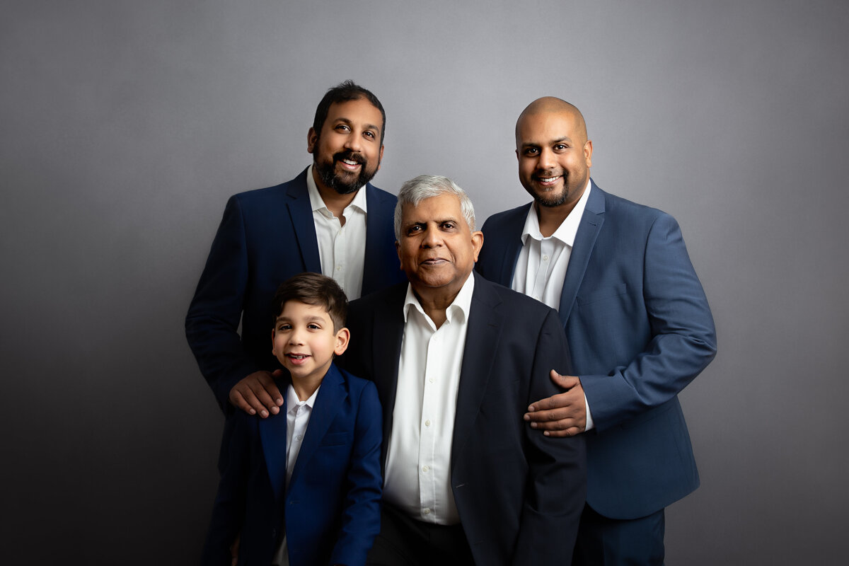 London studio portrait of a grandfather with his two sons and his grandson all dressed in navy blue.