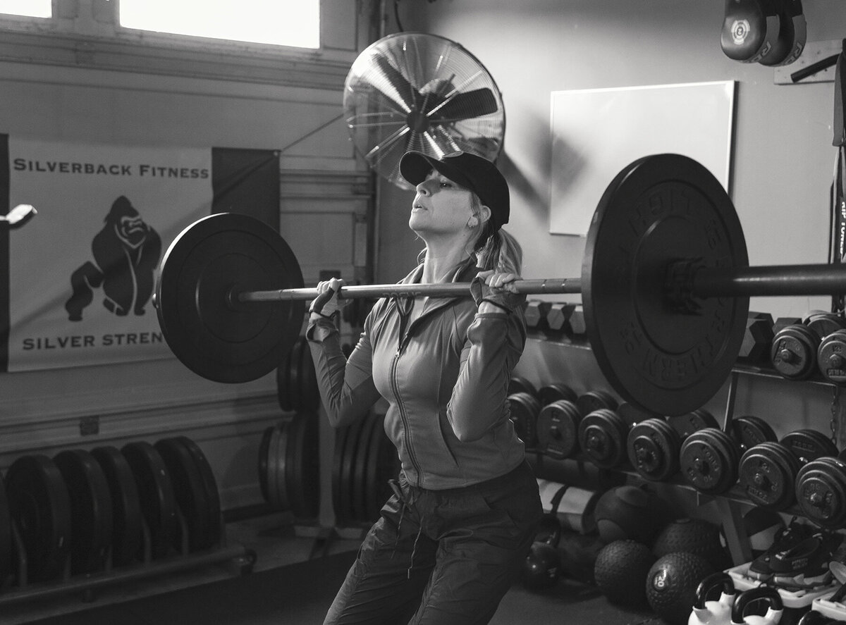 Woman is doing swats with a weighted barbell  at Silverback Fitness. She is being trained by Sarnia's best personal trainer Jim Stewart.