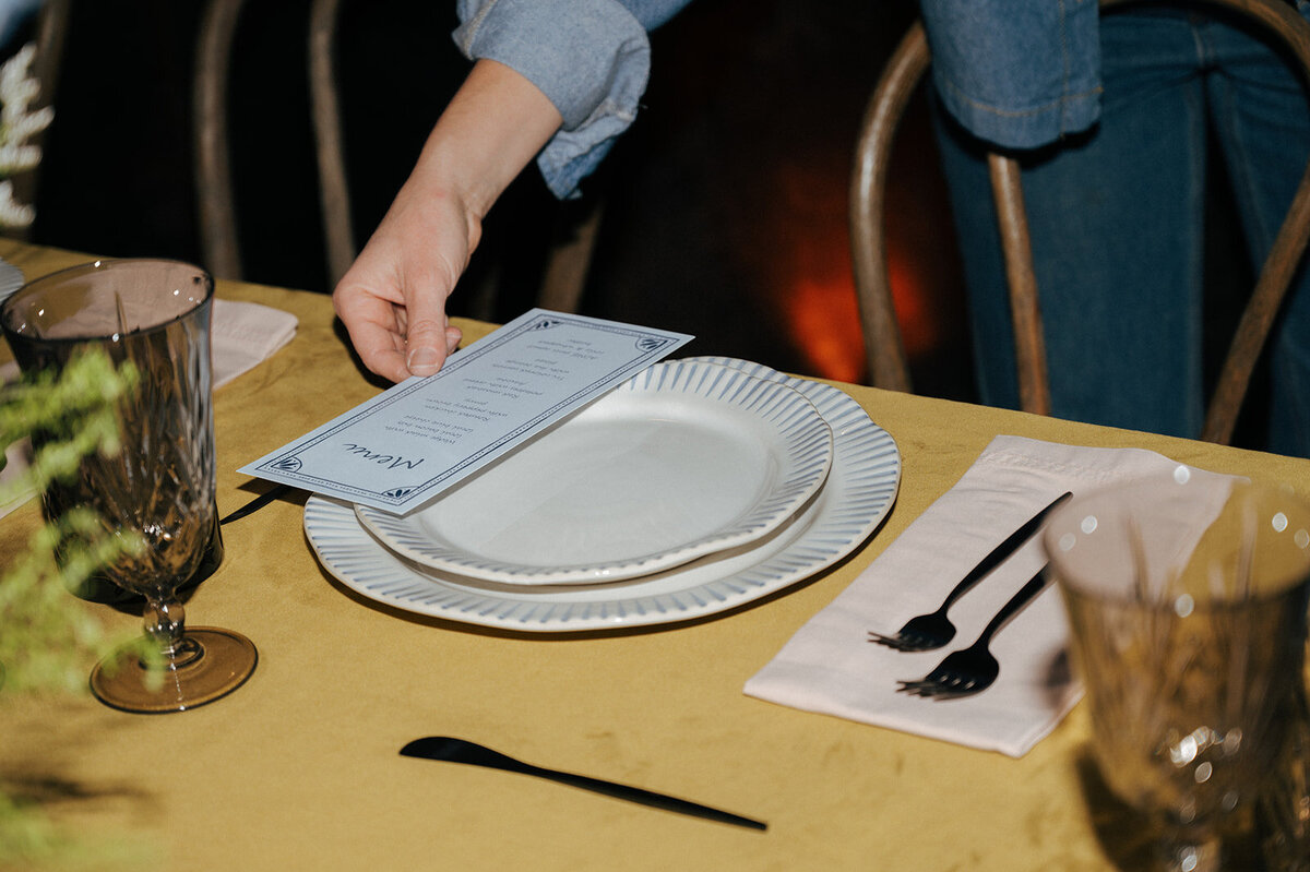 A hand placing a menu onto a table setting in preparation for an event planned by Perfect Thirds and Co 