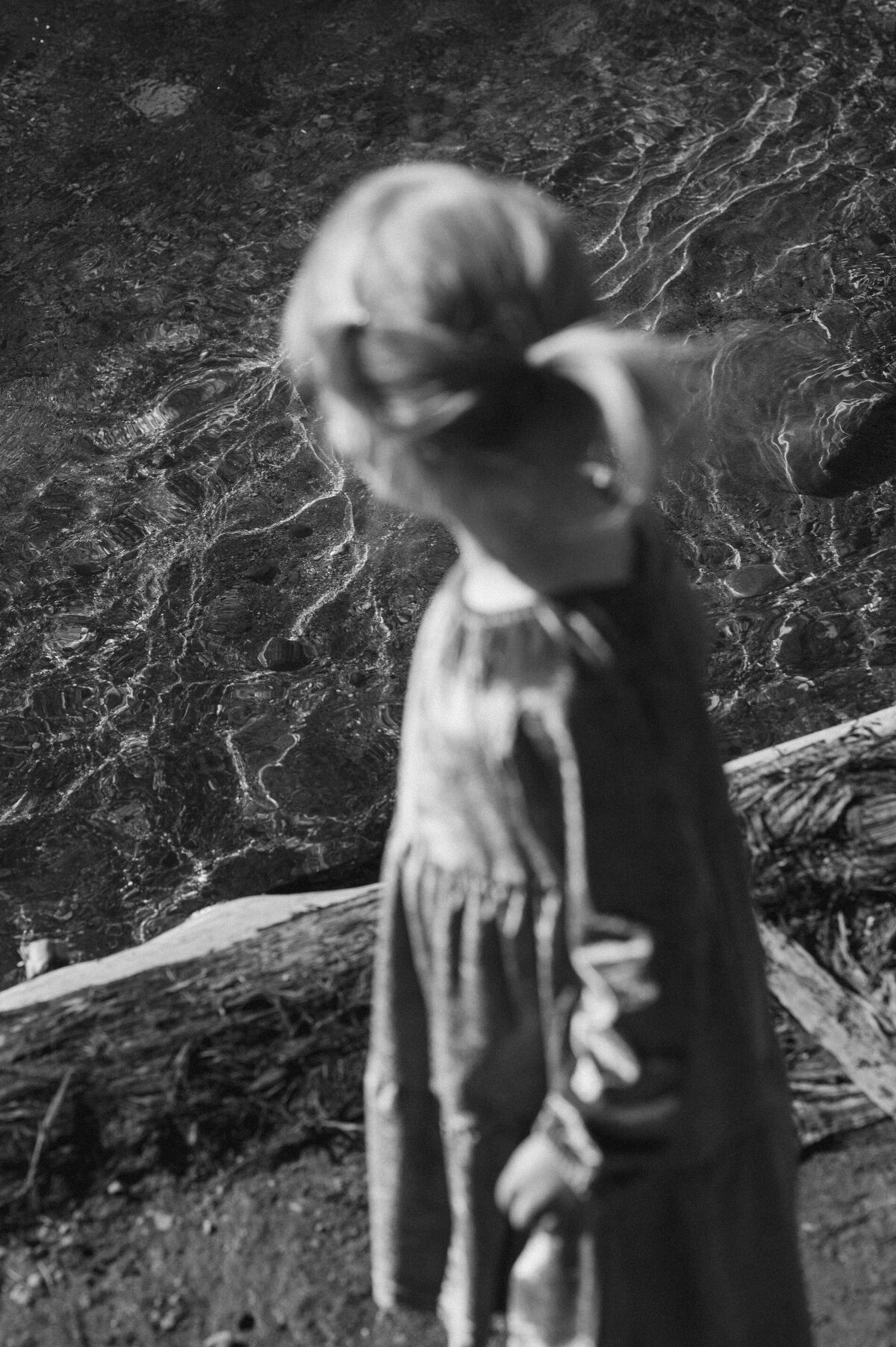 Little girl with ponytail and velvet dress stands near and looks at the flowing river
