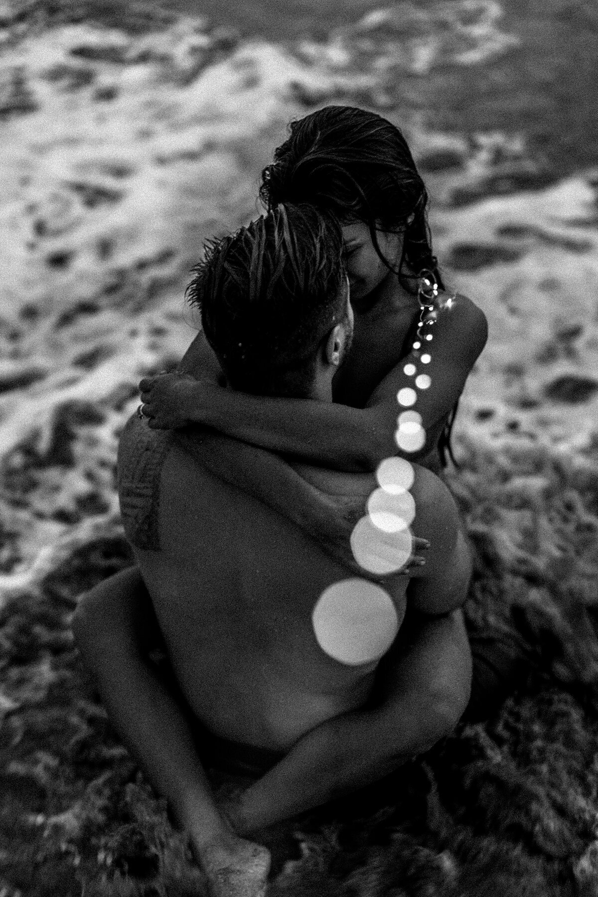 Creative lighting dances around an intimate portrait of a couple embracing in the ocean at sunset on Maui