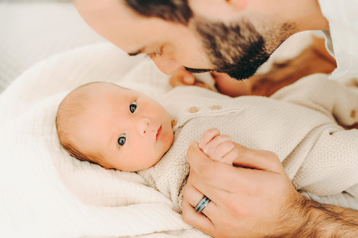 dad holds baby's hands  while baby looks at camera for newborn photos in jackson missouri