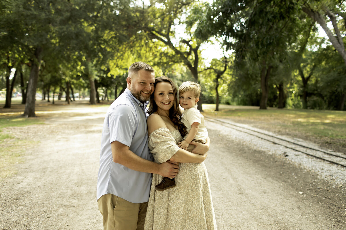 A romantic maternity photo of mom and dad standing in the park, with mom gently cradling her belly while dad wraps his arm around her, captured by Chunky Monkey Photography.