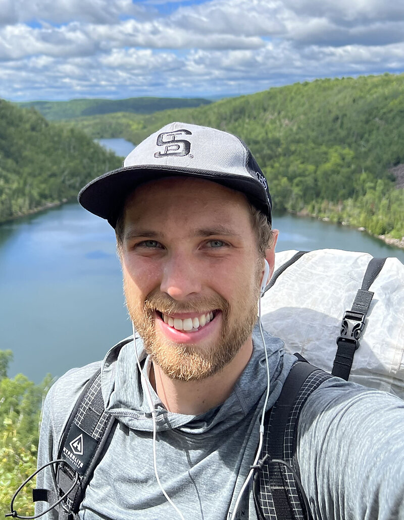 Before photo of client outdoors with scenic lake and forest background, smiling during a hike before his online dating portrait session with Shannon Kathleen Photography.