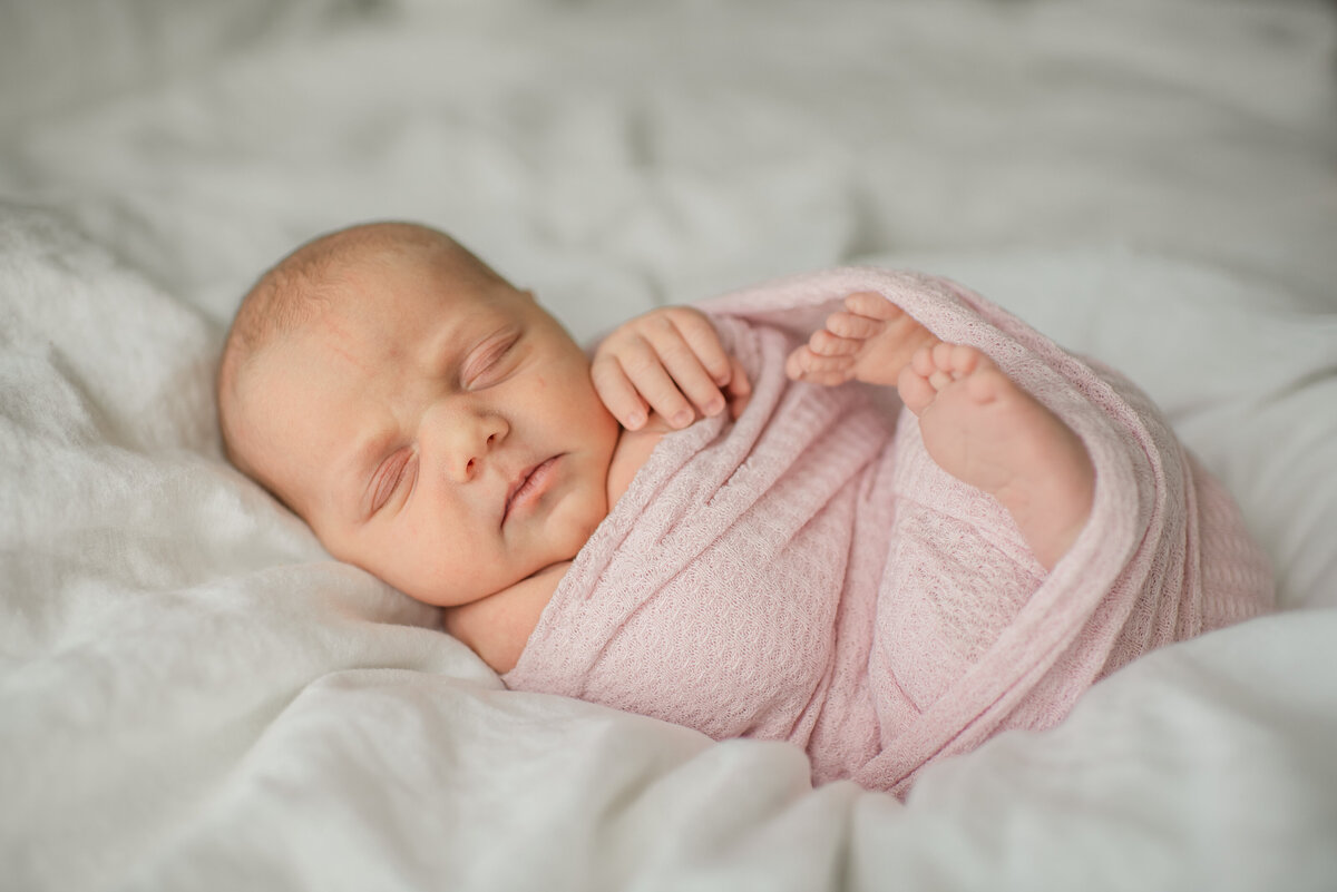 sleepy newborn girl in blush pink swaddle on a fluffy bed - maryland newborn photographer