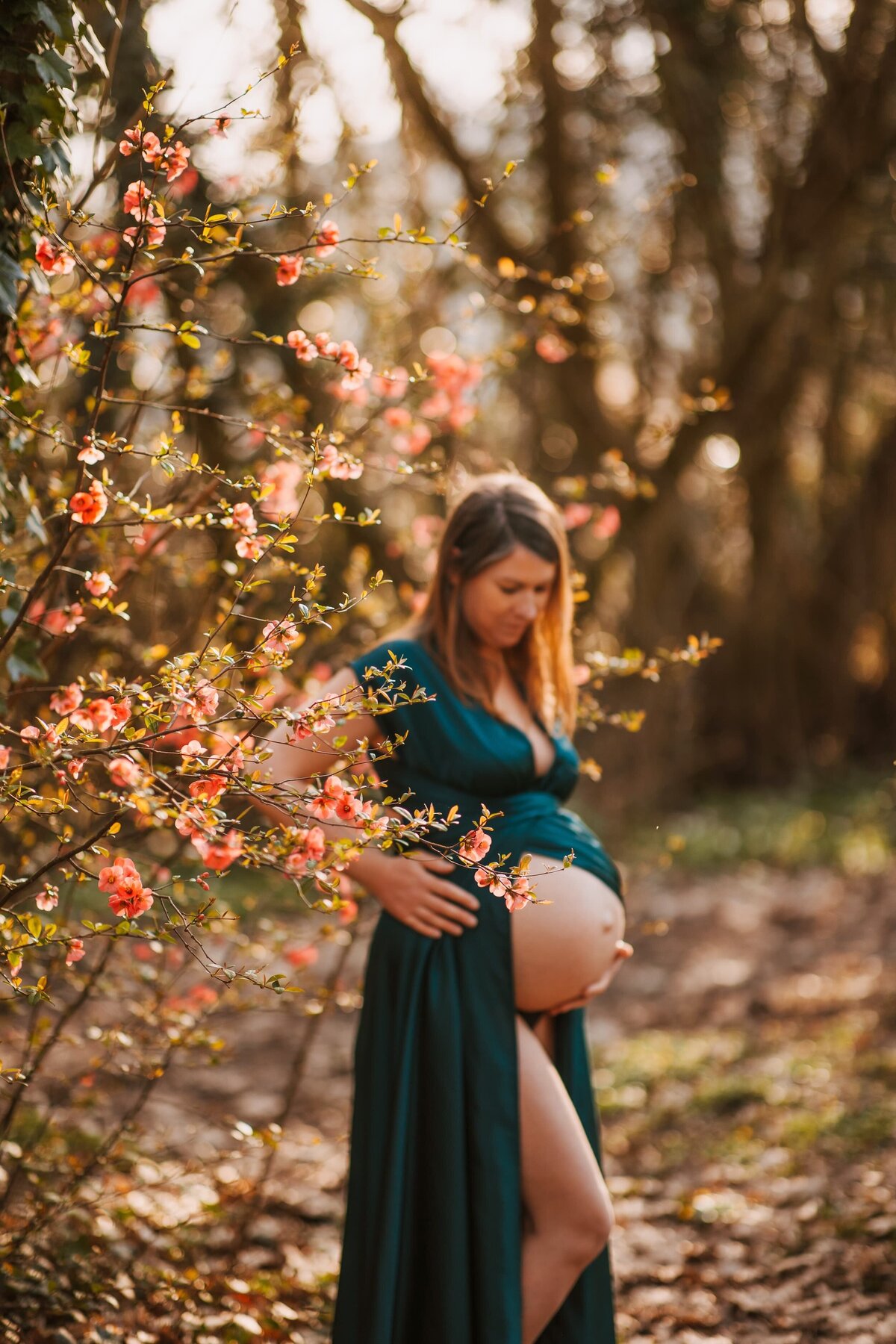 photo de grossesse femme en robe verte dans la forêt regardant son ventre