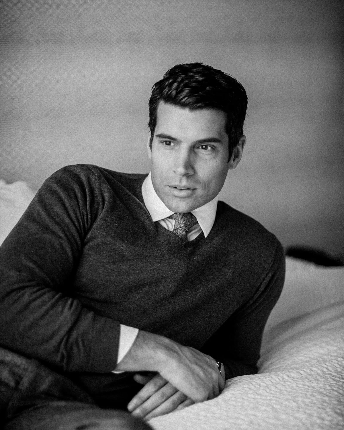 A man in a sweater leaning back on a bed.
