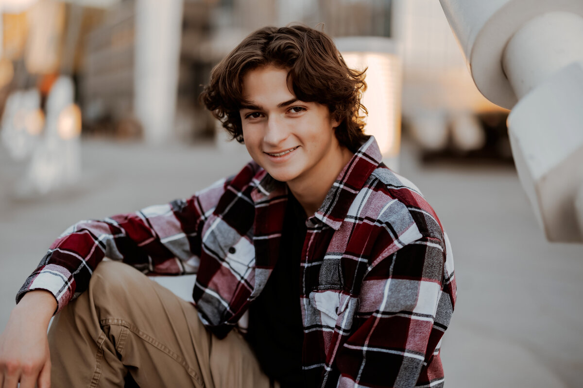 Senior boy wearing a plaid shirt posing on stairs in downtown Denver for his Senior session.