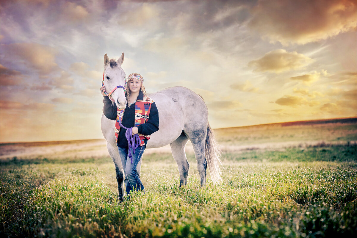 Native American High School Senior holding her white horse in the field.