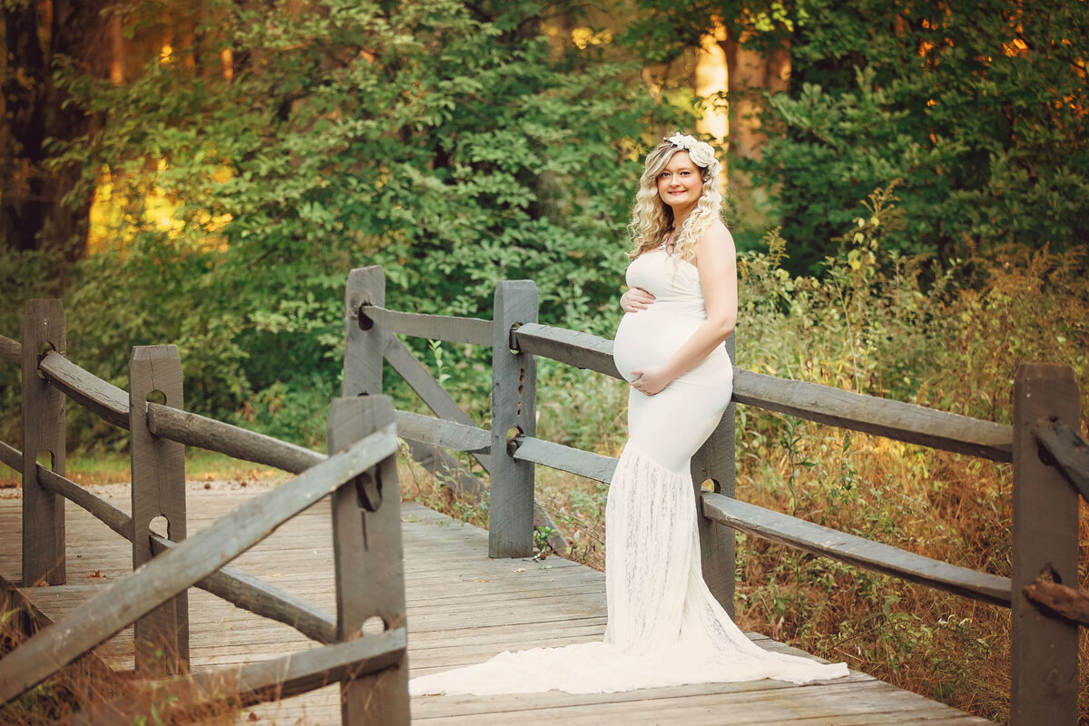 pregnant woman standing on the wooden bridge holding her belly during her maternity session in NJ park