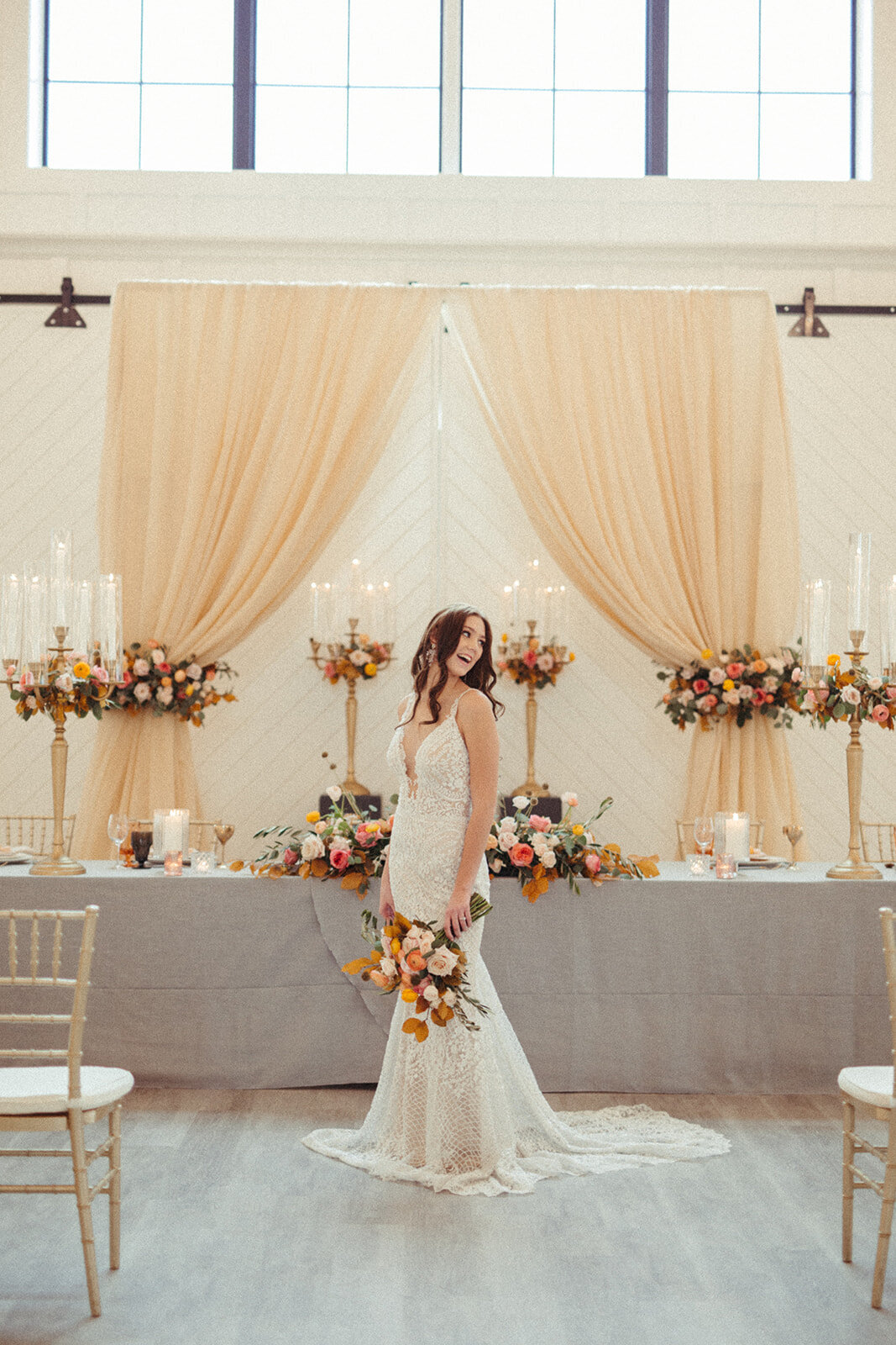A bride wearing a white wedding gown holds a bouquet in front table with gray linen, candlesticks and flowers.