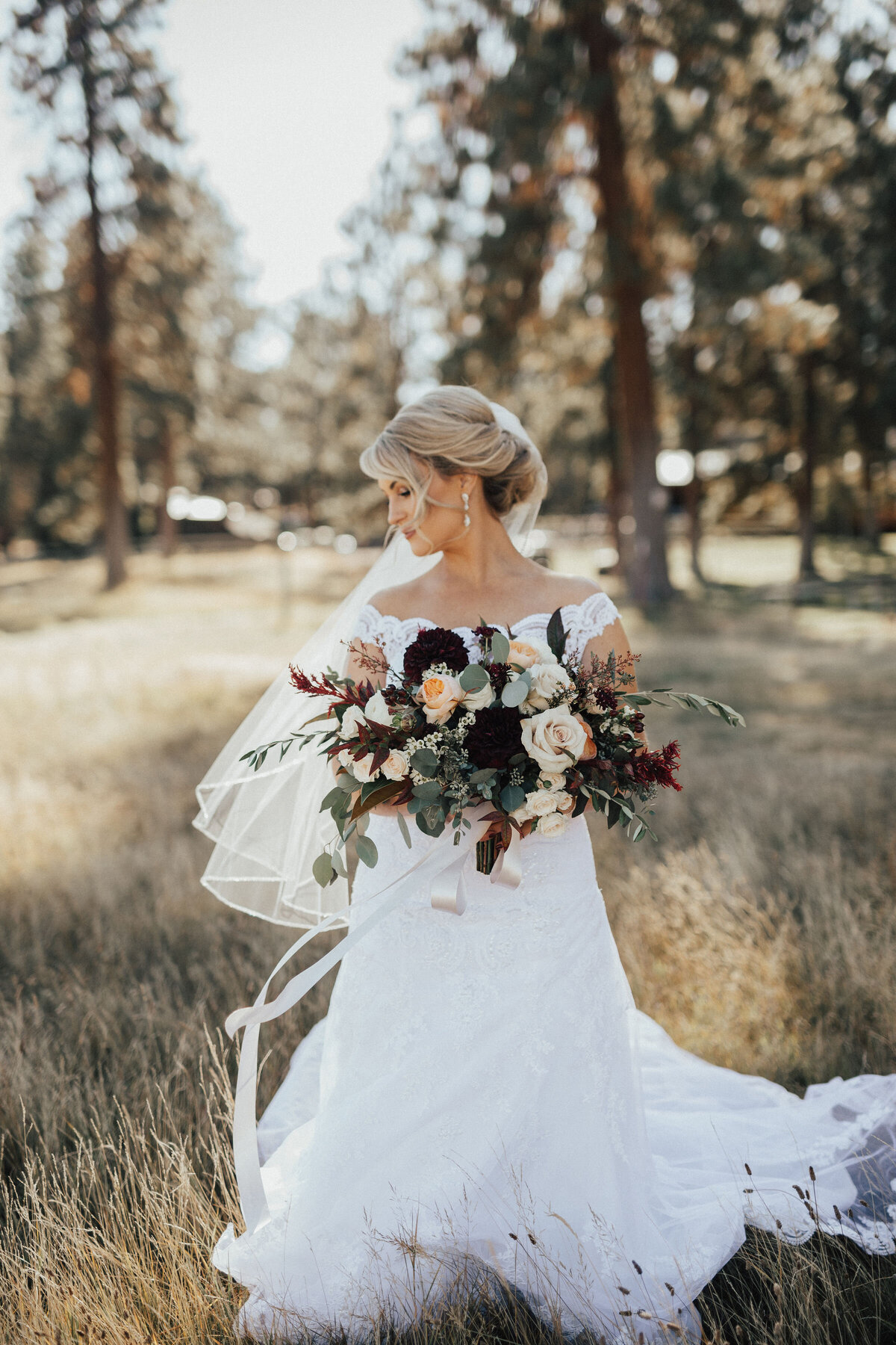 Bride in field in Sisters holding a wedding bouquet of burgundy and blush roses