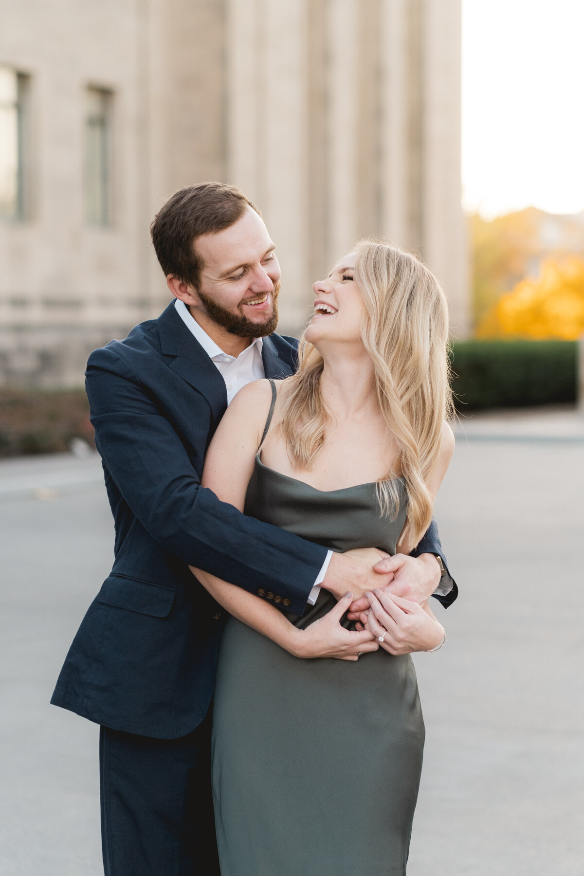couple wearing emerald green and navy blue embracing in front of engagement session at the Nelson-Atkins Museum