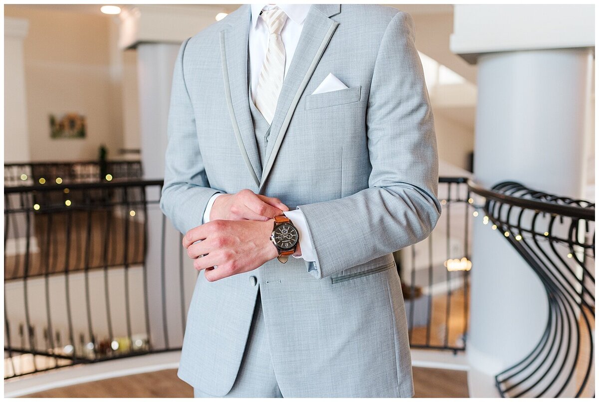 close up photo of groom in a grey suit adjusting his cuff links while showing off his watch