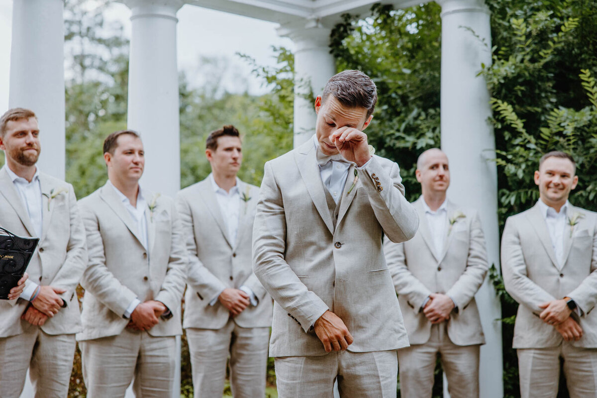 The groom wipes away a tear as he watches his future wife walk down the aisle. 