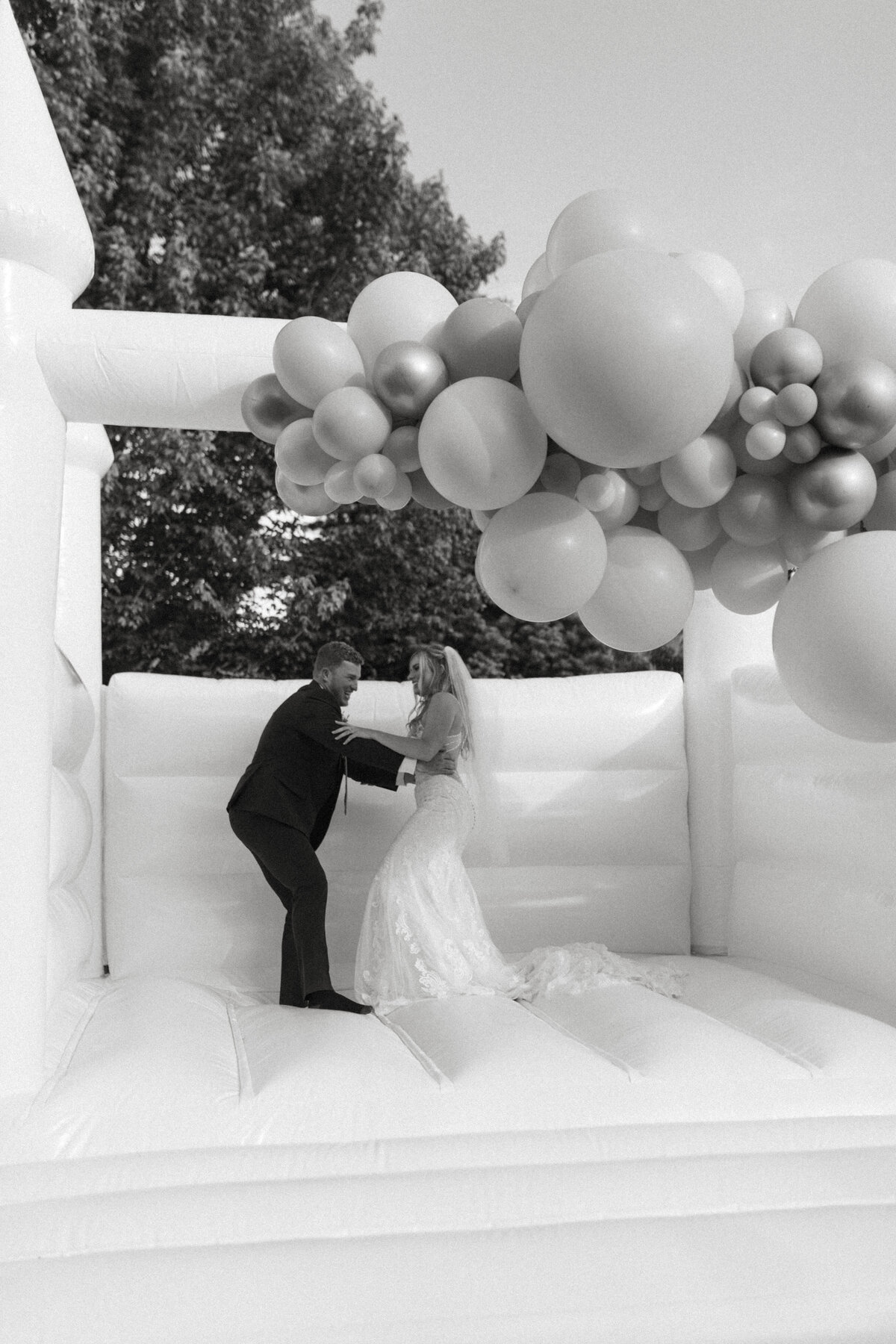 Bride and groom jumping in a white bouncy house IN BLACK AND WHITE.