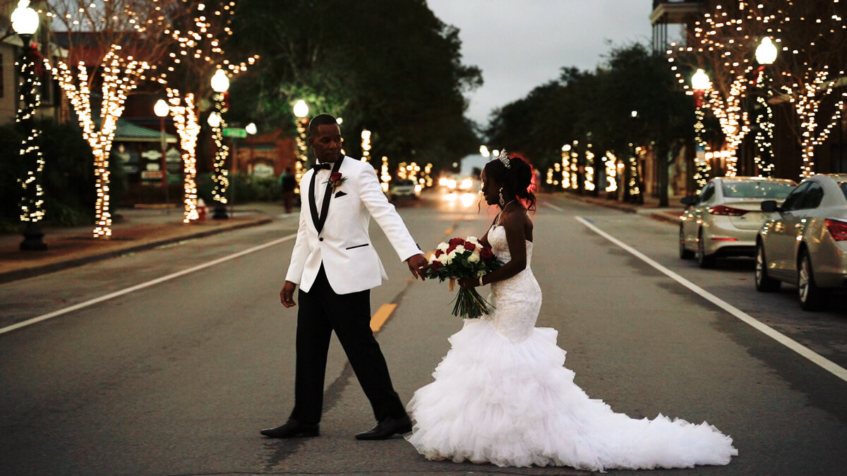 Bride and groom walk down the street holding hands.