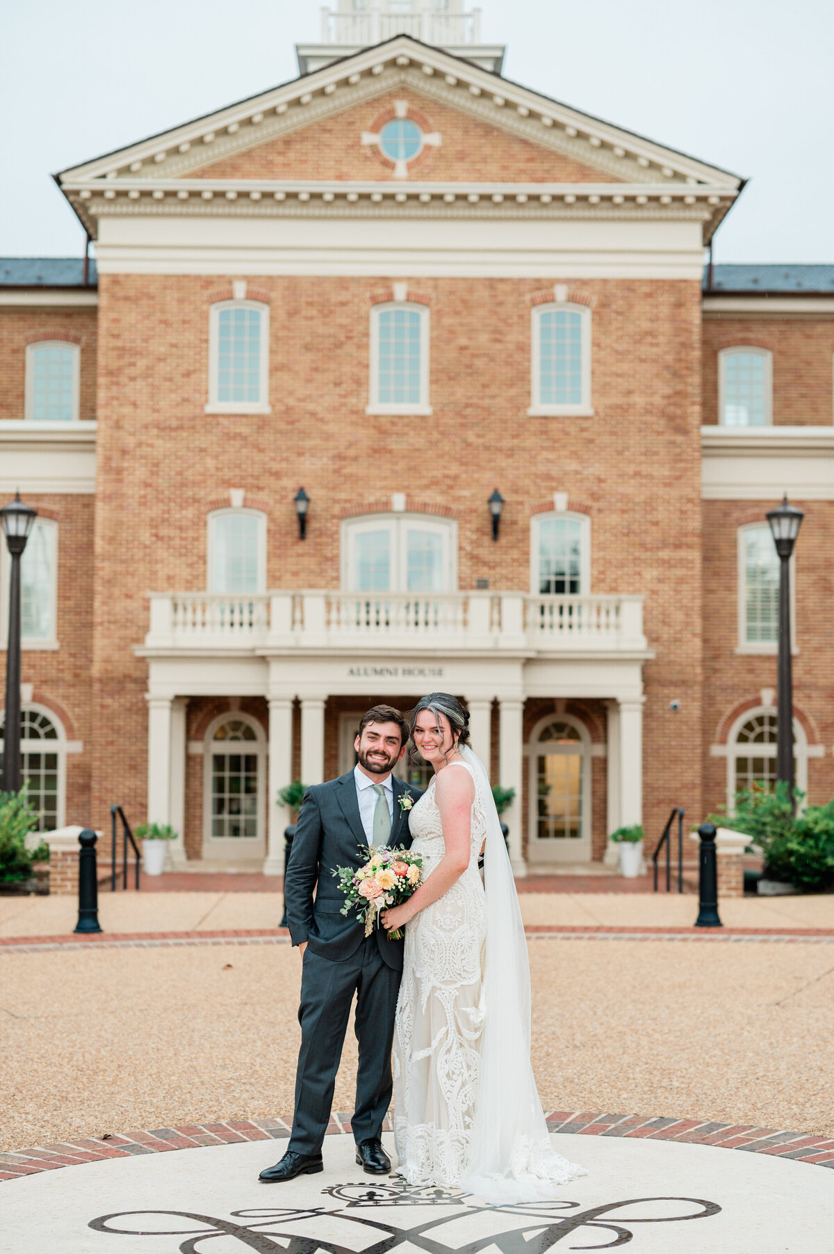 A wedding couple standing close together in front of a mansion