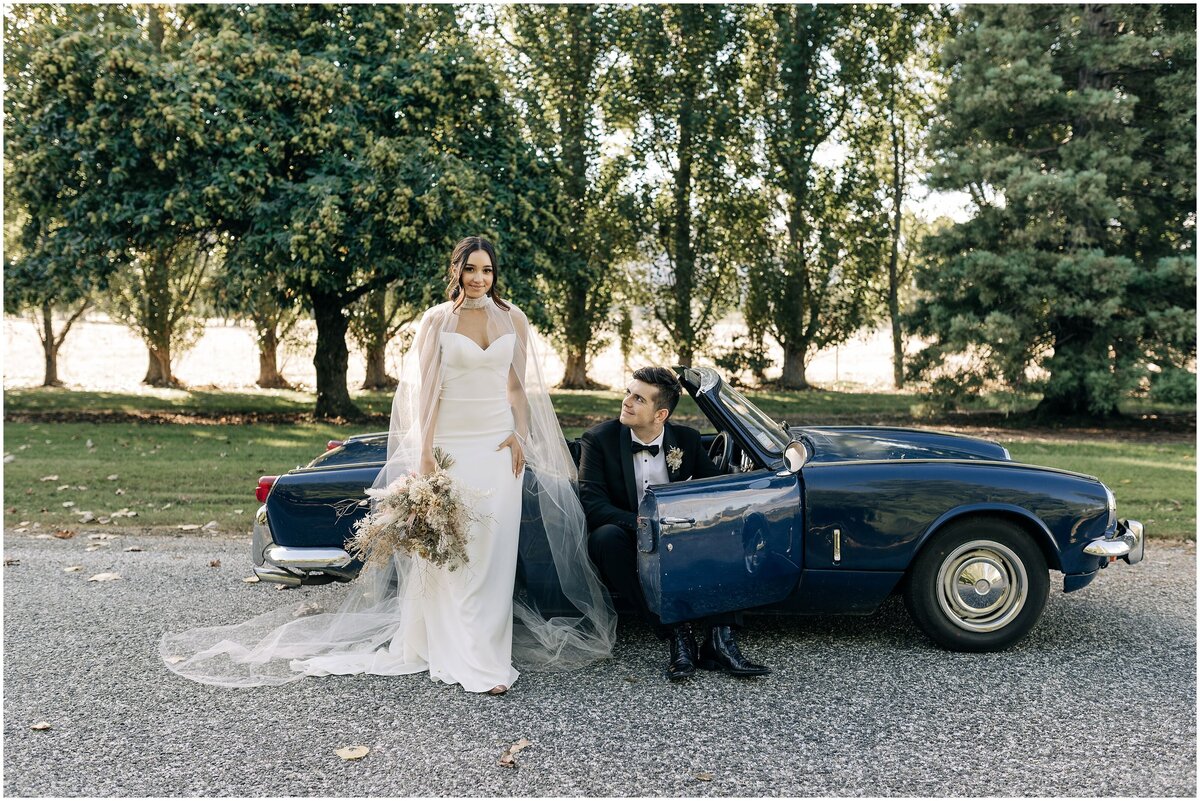 bride and groom with white cape editorial elegant on blue convertible queenstown nz tuxedo with green trees