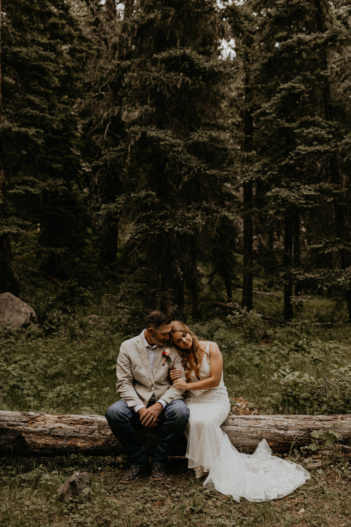 bride and groom sitting together closely in a forest