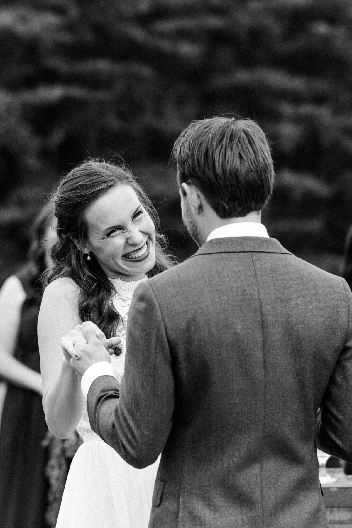 Bride and groom exchanging vows outdoors, captured in black and white. The emotional moment is framed by a serene natural backdrop, emphasizing their connection.