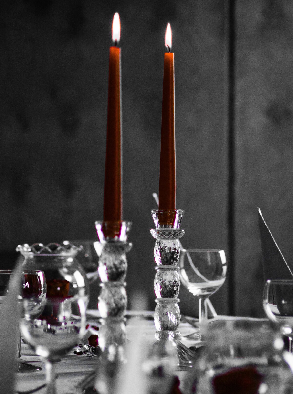 Two red candles in glass candlesticks are placed on a table set for a party.