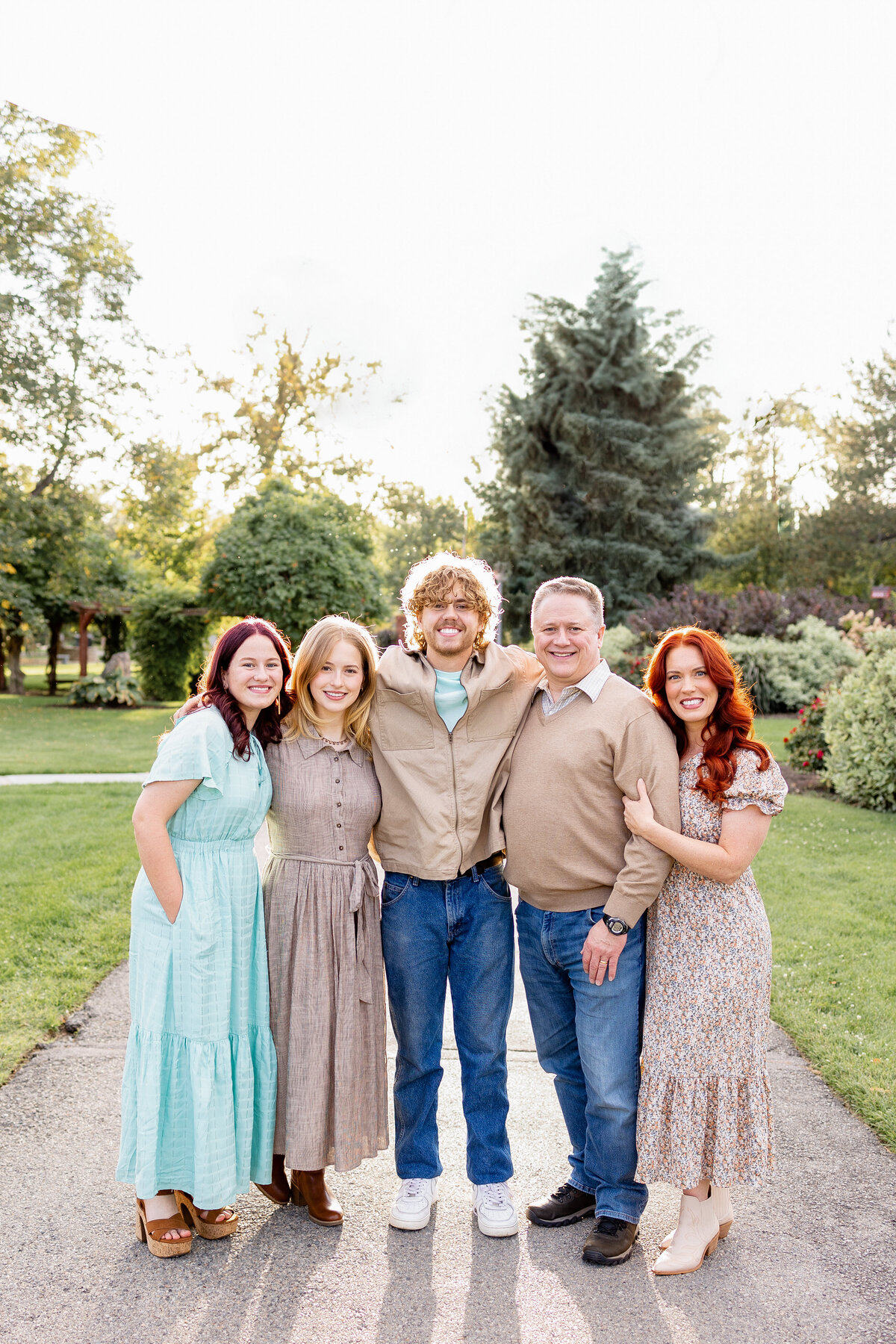 A family of five walks along a scenic pathway, framed by lush trees and a beautifully landscaped park.