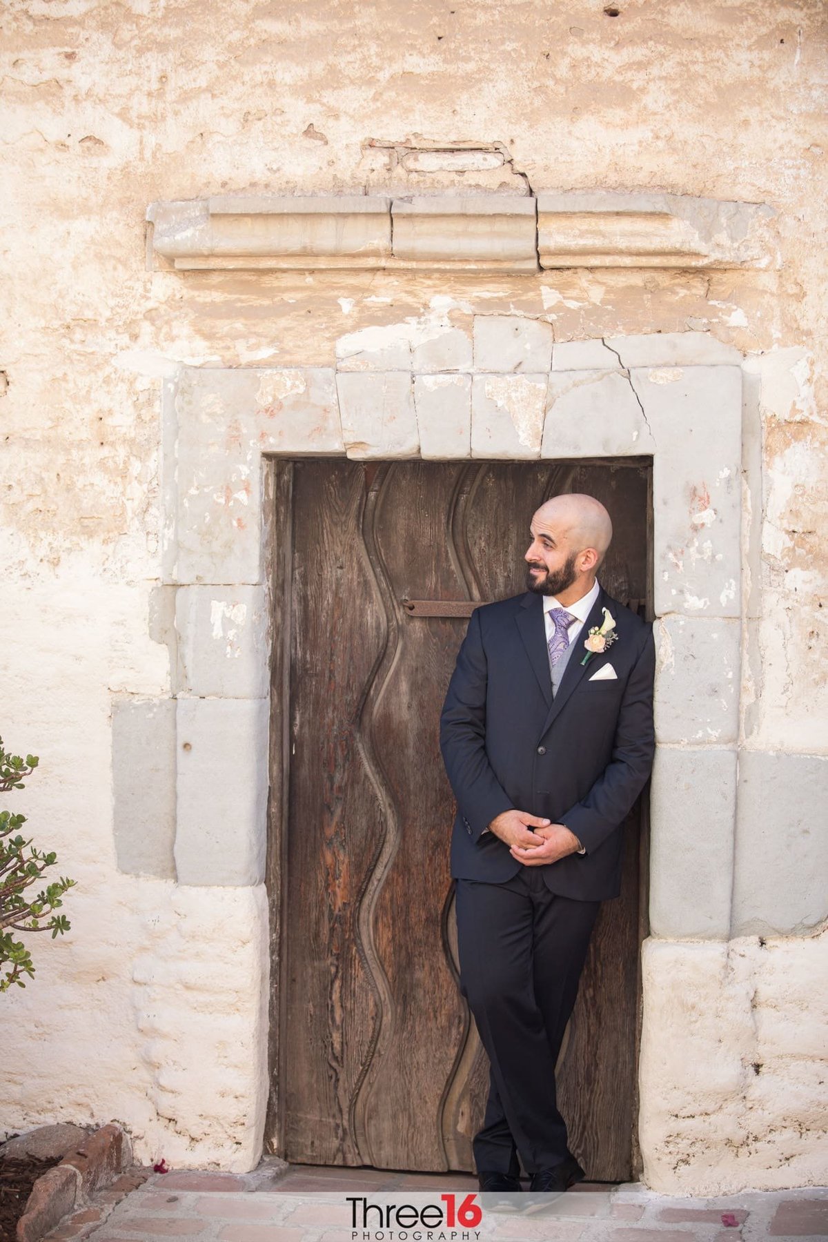 Groom leans against a door as he poses for photos