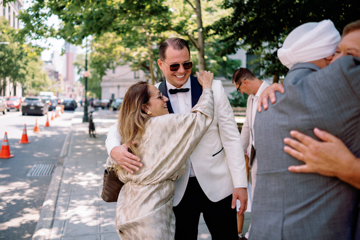 Groom smiling as he embraces a family member outside on the streets of New York City, captured candidly during Japna and Chris’s Hotel Chelsea elopement by NYC wedding photographer Perry Hancock.