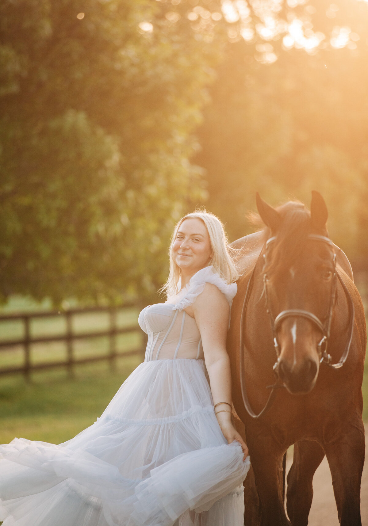 blonde woman in blue dress leaning against her horse
