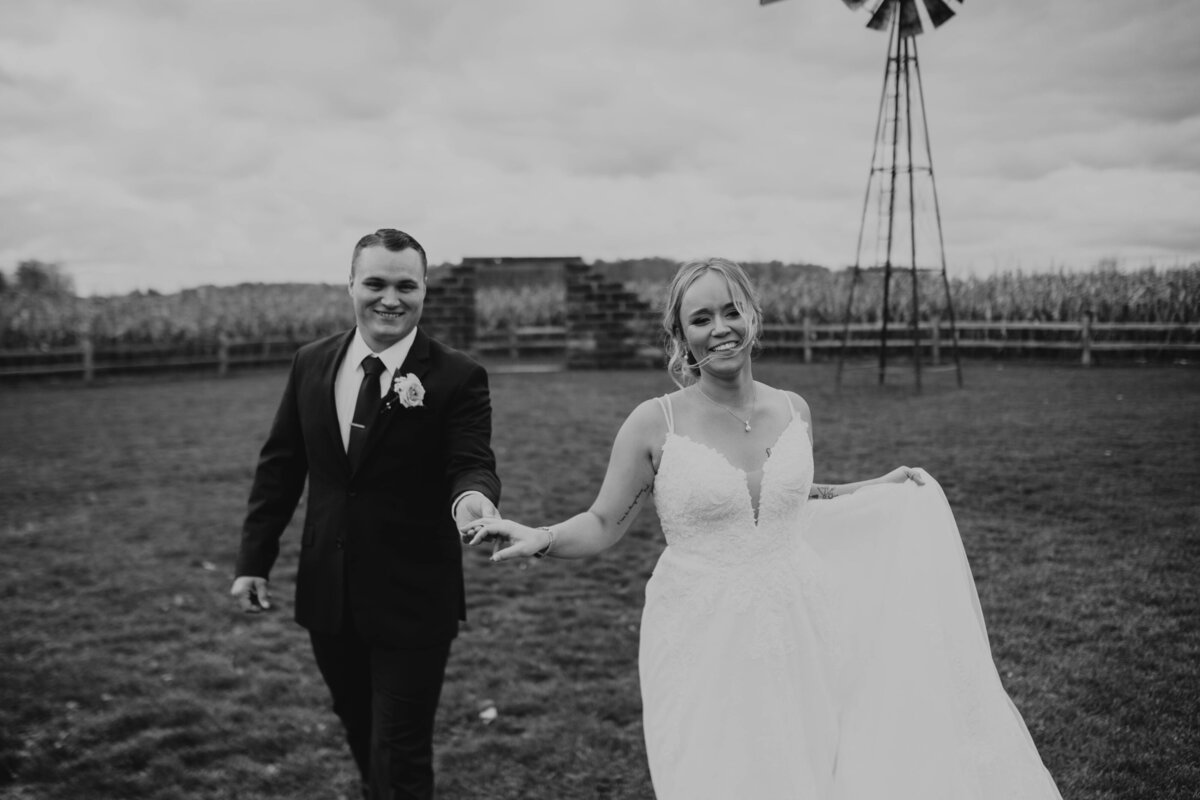 black and white photo of bride and groom holding hands walking towards the camera