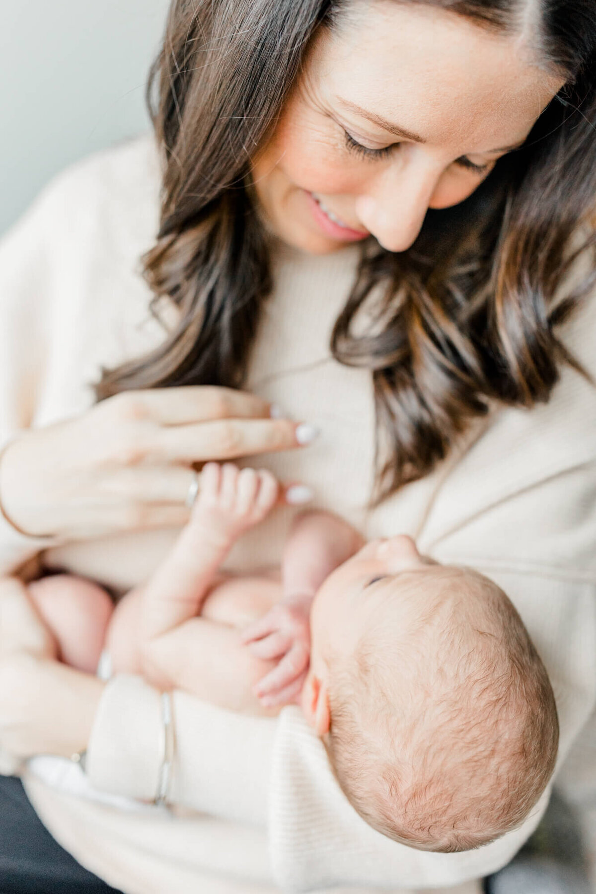 Mother smiles down at her newborn in her arms while he grasps her finger