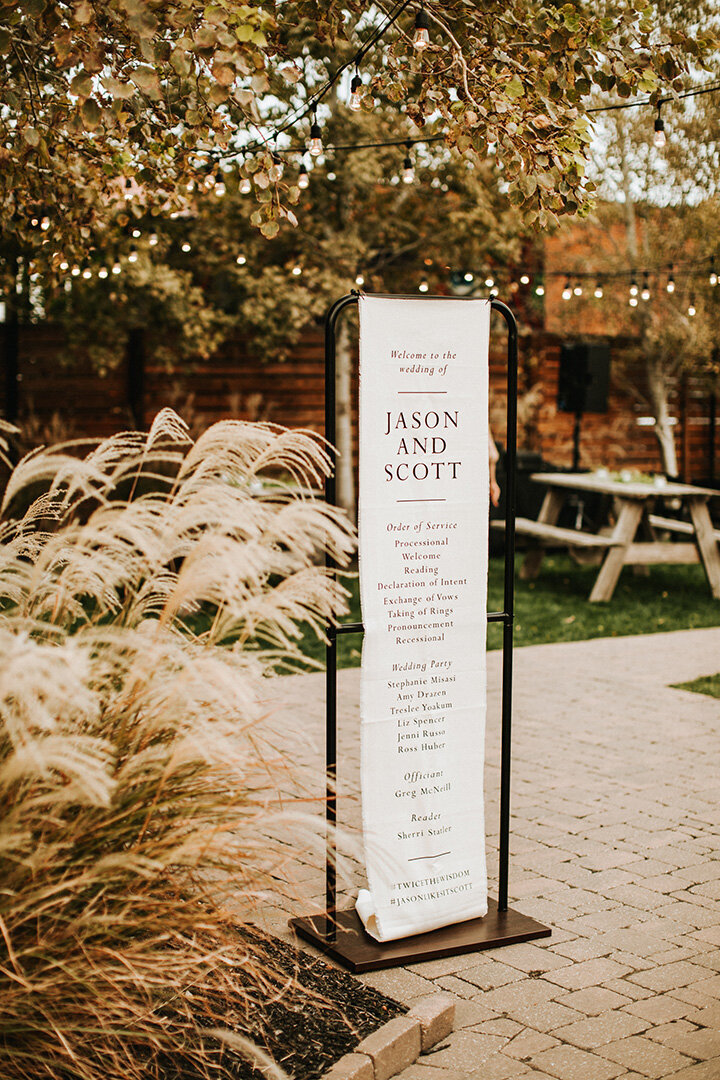 White wedding banner with black font hanging on black metal stands in quart yard.