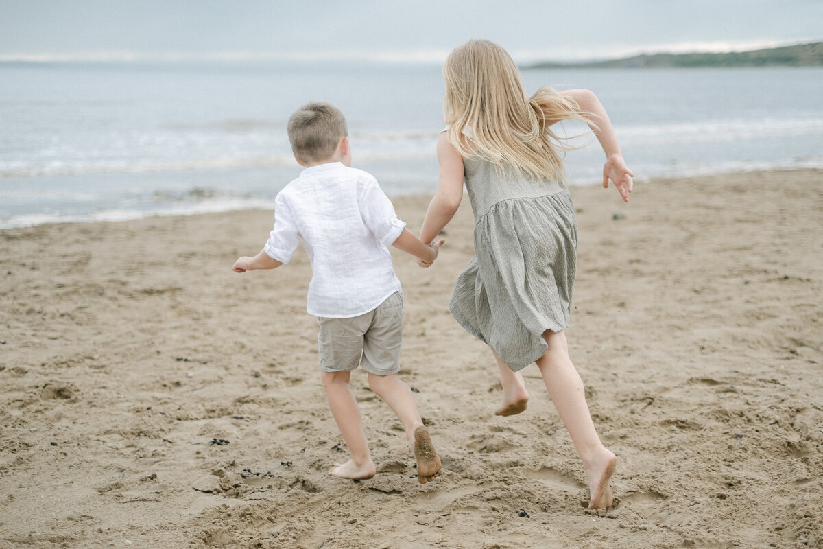 Two children run along the sand during an outdoor family photoshoot at the beach