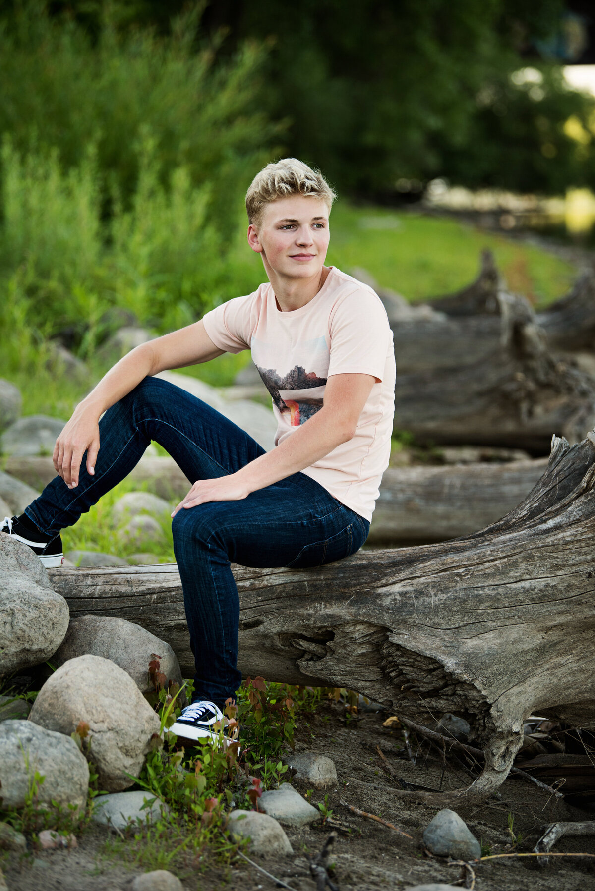 senior picture of boy sitting on driftwood in nature wearing jeans and t-shirt