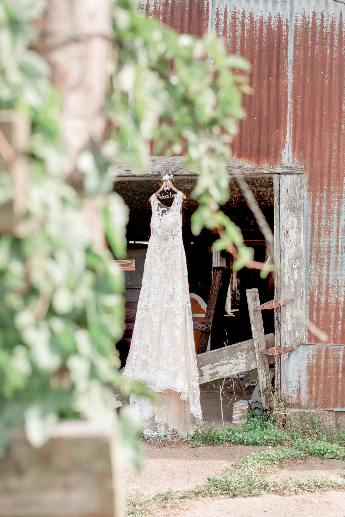 The brides dress, framed with leaves,  hangs in the doorway of the metal barn