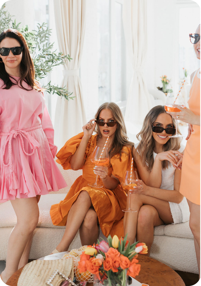 3 girls in orange and pink sipping on fun beverages during a female led social media photoshoot.