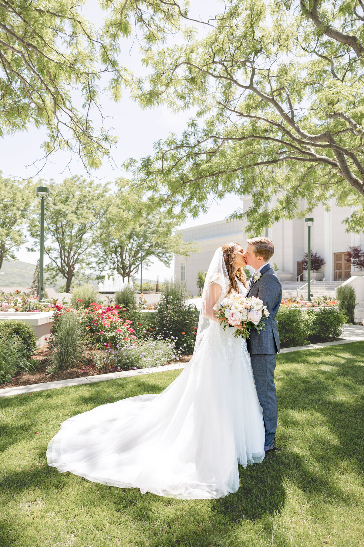 The bride and groom stand on the lush green lawn, sharing a romantic kiss in front of the Bountiful Utah LDS Temple.