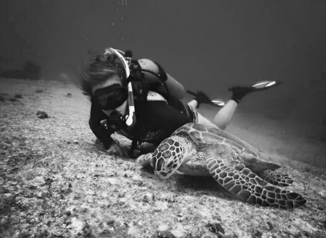 Nicole is pictured in scuba gear on the sea floor next to a large sea turtle.