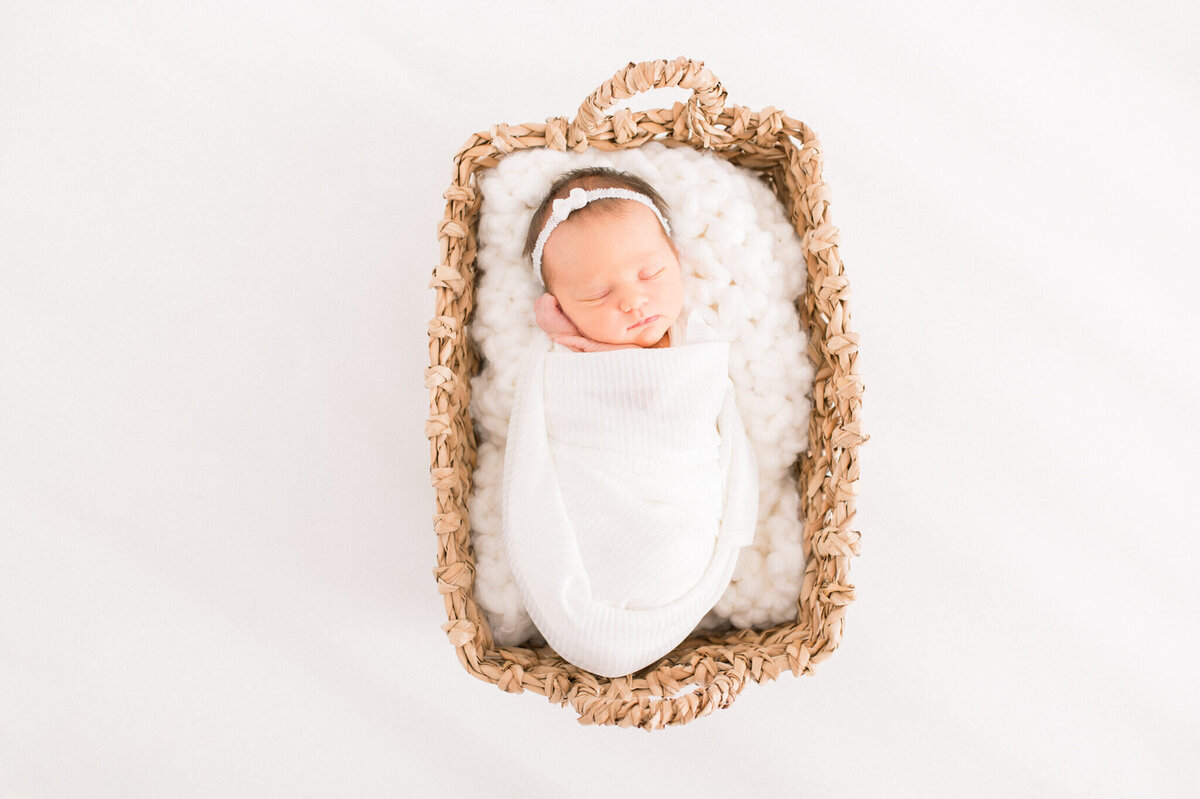 Baby girl in wicker basket on a white backdrop captured in studio by Niagara newborn photographer